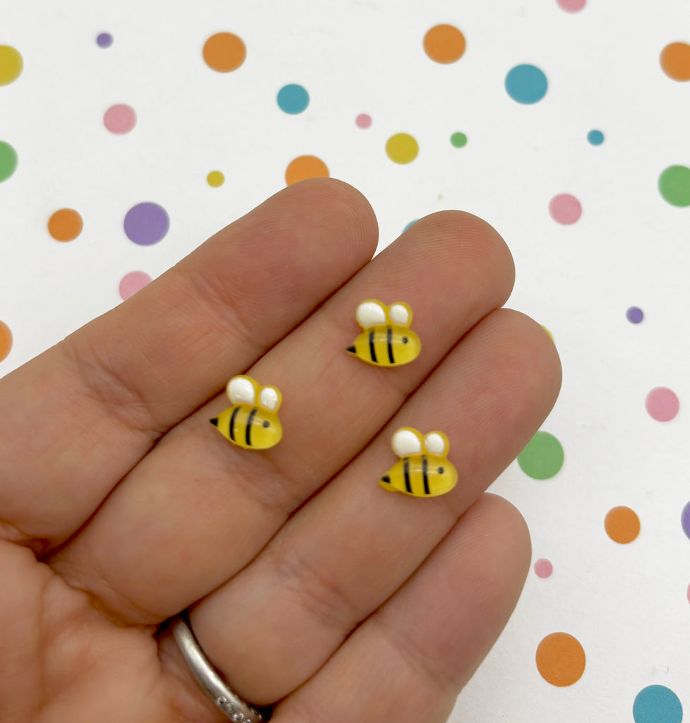 a hand holding a pair of tiny yellow and white bees