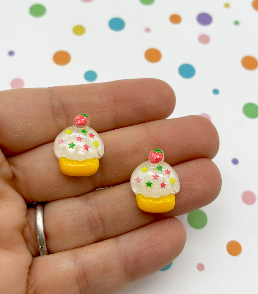a hand holding two tiny yellow and white cupcakes