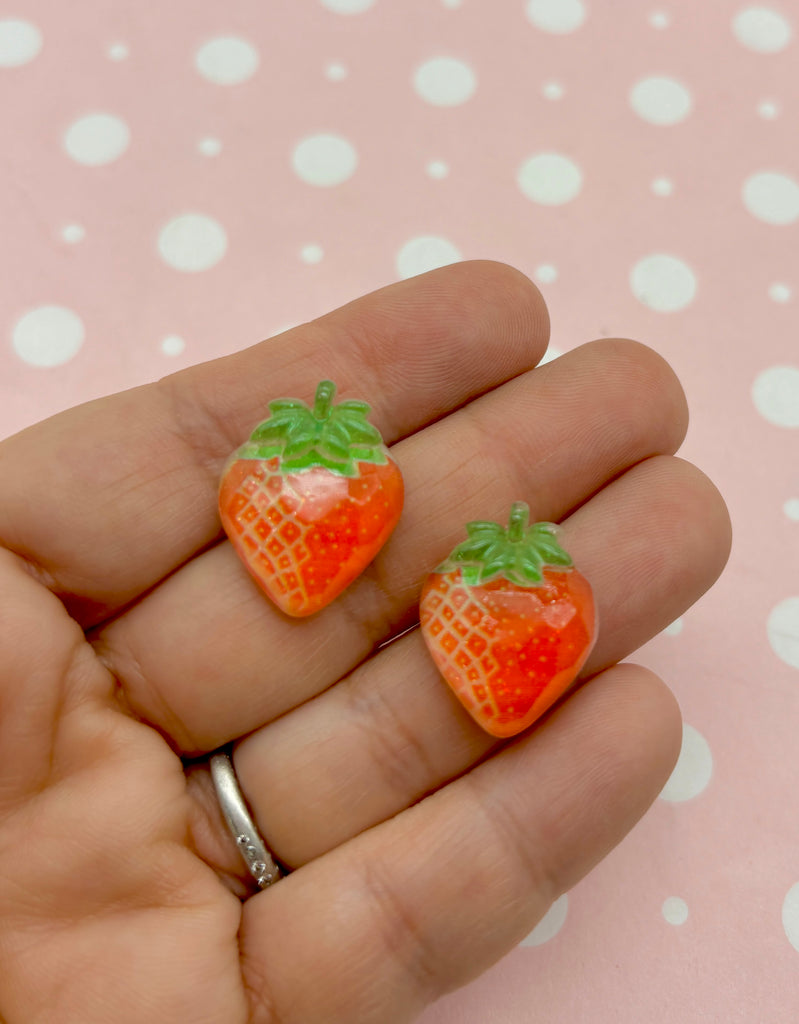 a hand holding two small orange fruit shaped earrings