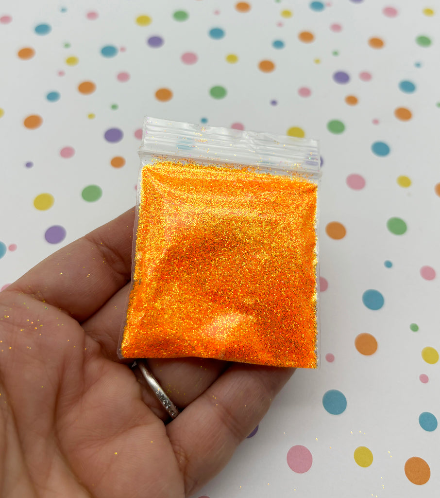 a hand holding a small orange bag of glitter