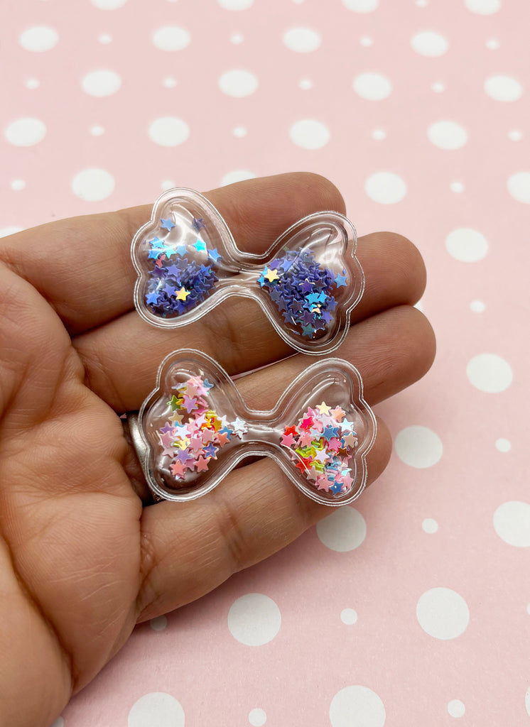 a person holding two small bows with glitter on them