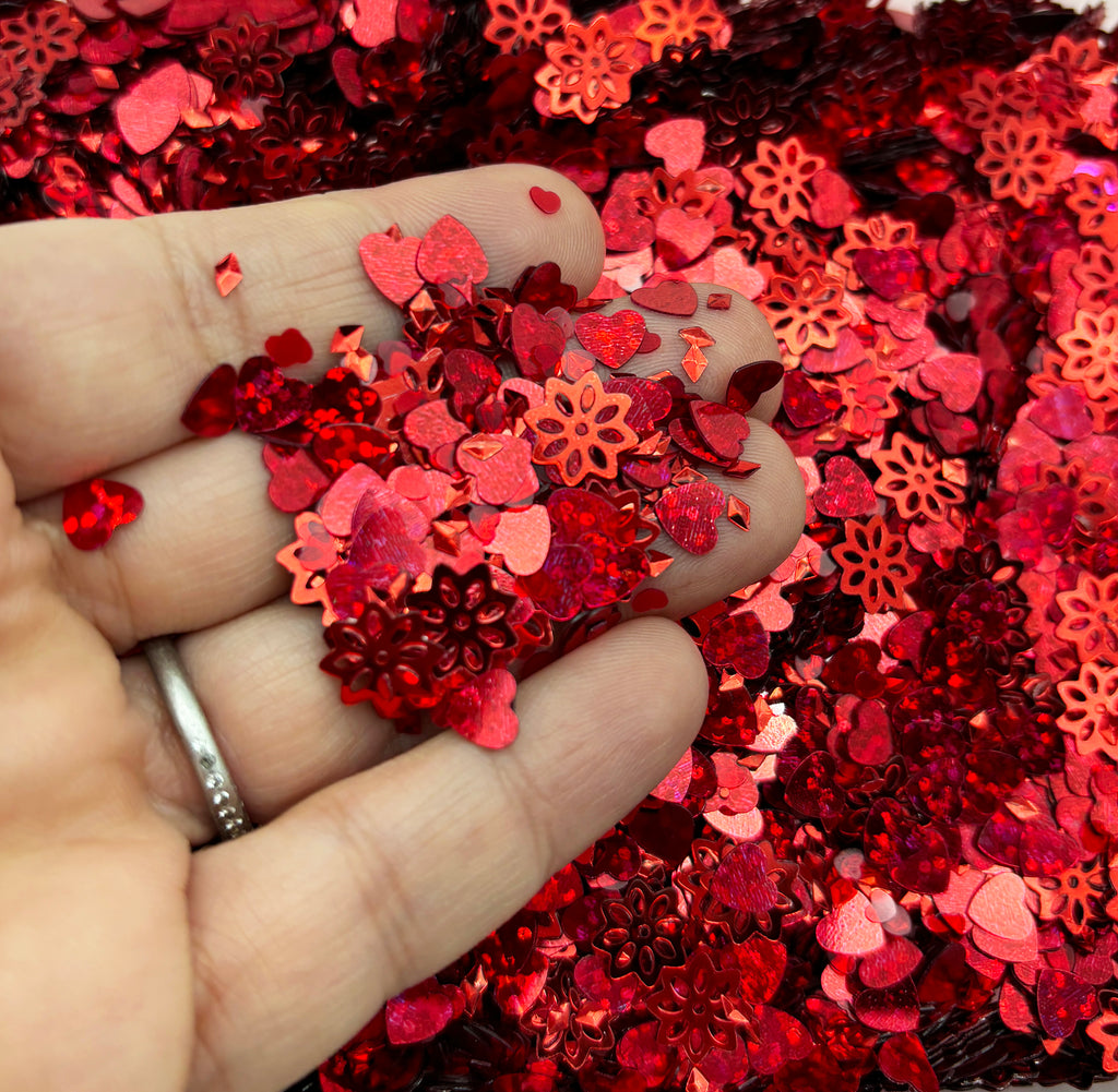 a hand holding a ring over a pile of red sequins