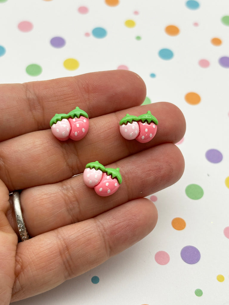a hand holding a pair of pink and green strawberry shaped earrings
