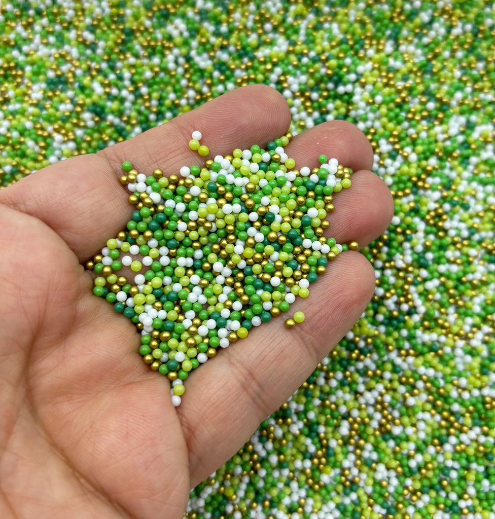 a hand holding a handful of tiny green and white beads