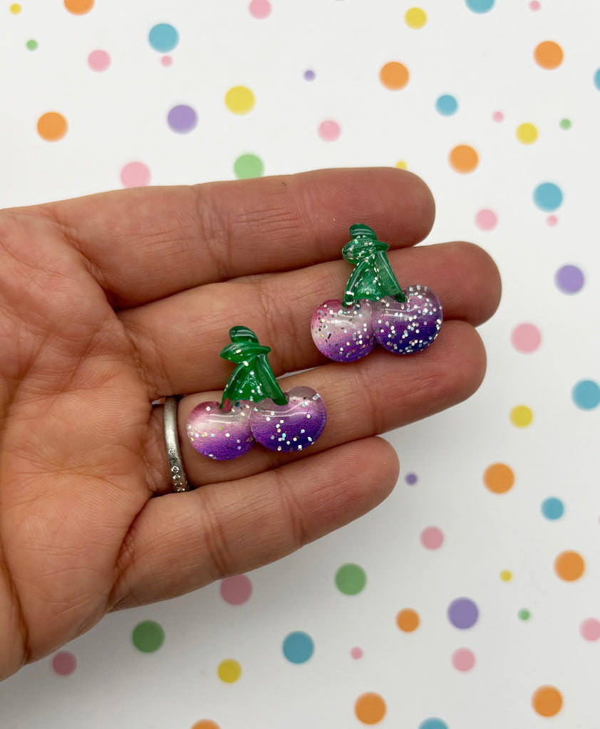 a hand holding a pair of purple and green christmas decorations