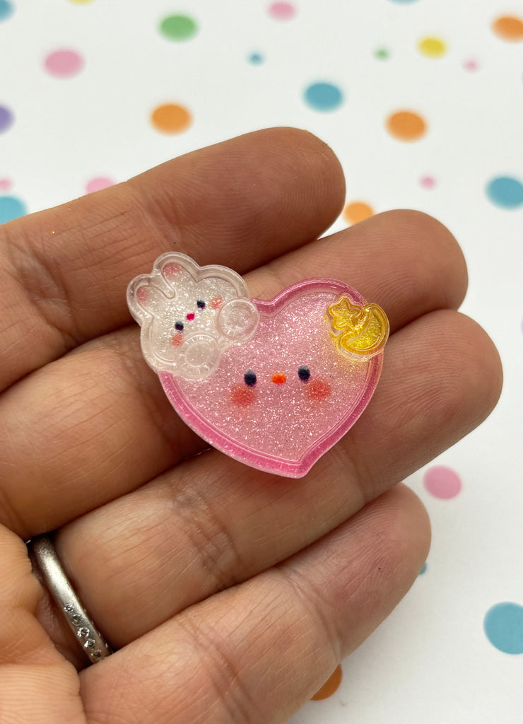 a hand holding a small pink heart shaped brooch