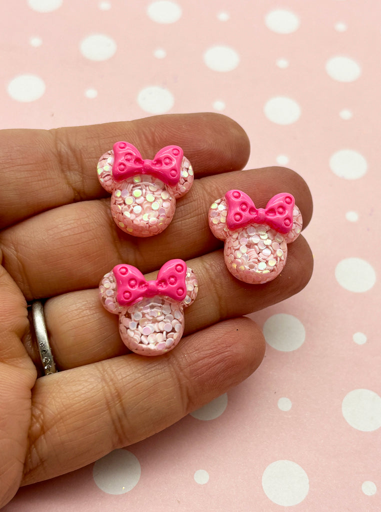 a hand holding three pink minnie mouse earrings