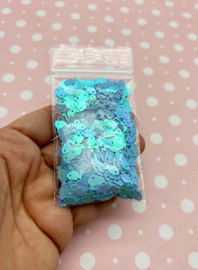 a hand holding a bag of blue and green sequins