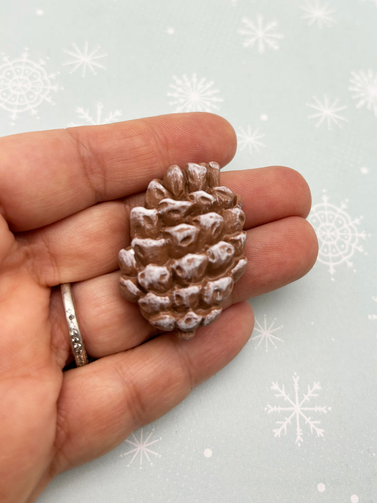 a hand holding a tiny pine cone ring