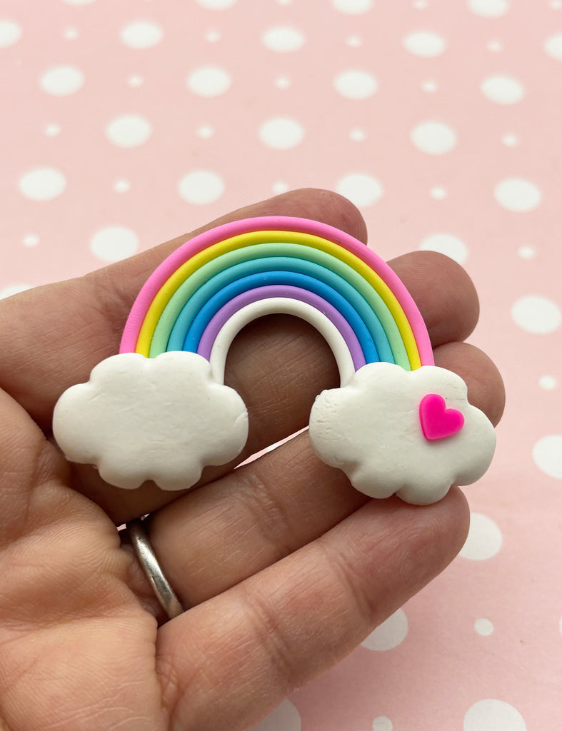 a hand holding a rainbow and cloud brooch