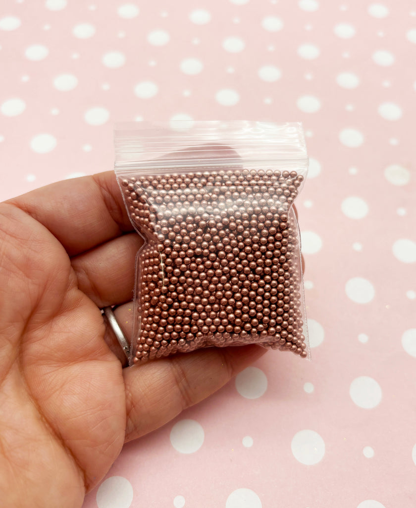 a hand holding a bag of beads on a pink background
