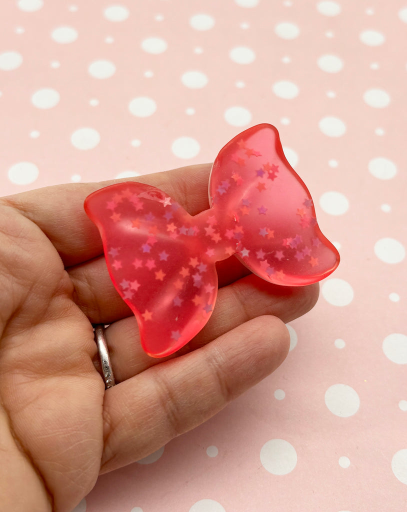 a hand holding a pink bow brooch on a pink background