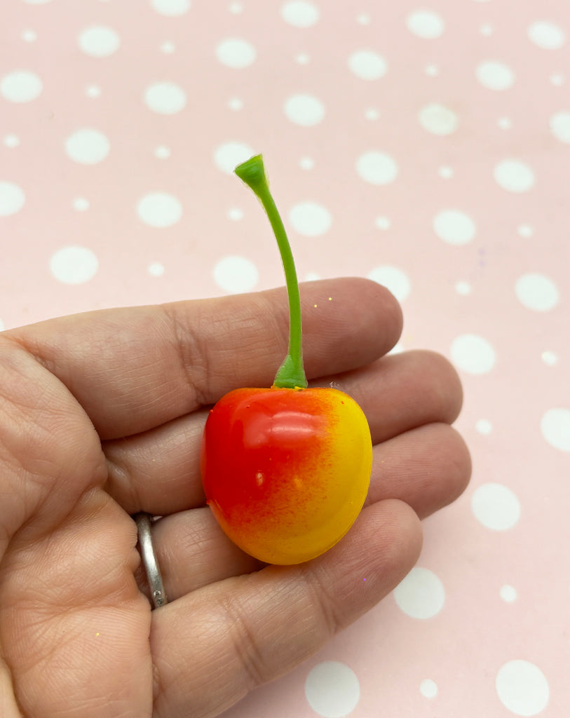 a hand holding a tiny cherry on a pink background