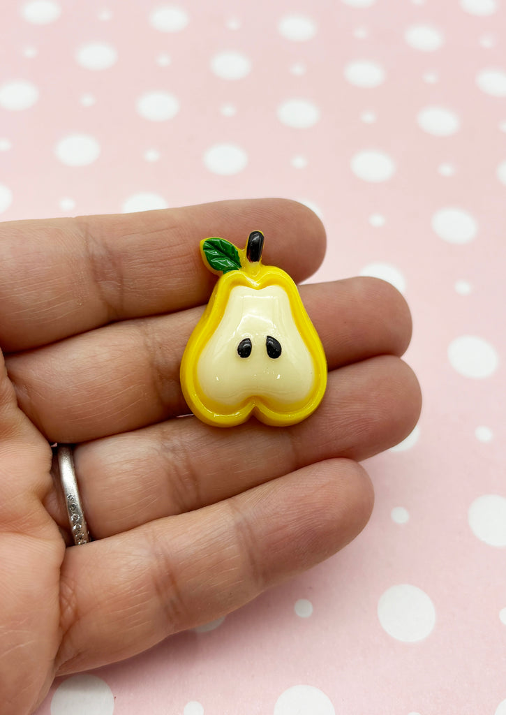 a hand holding a yellow and white apple brooch