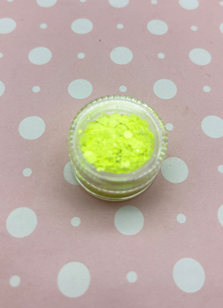 a small container of yellow glitter on a pink background