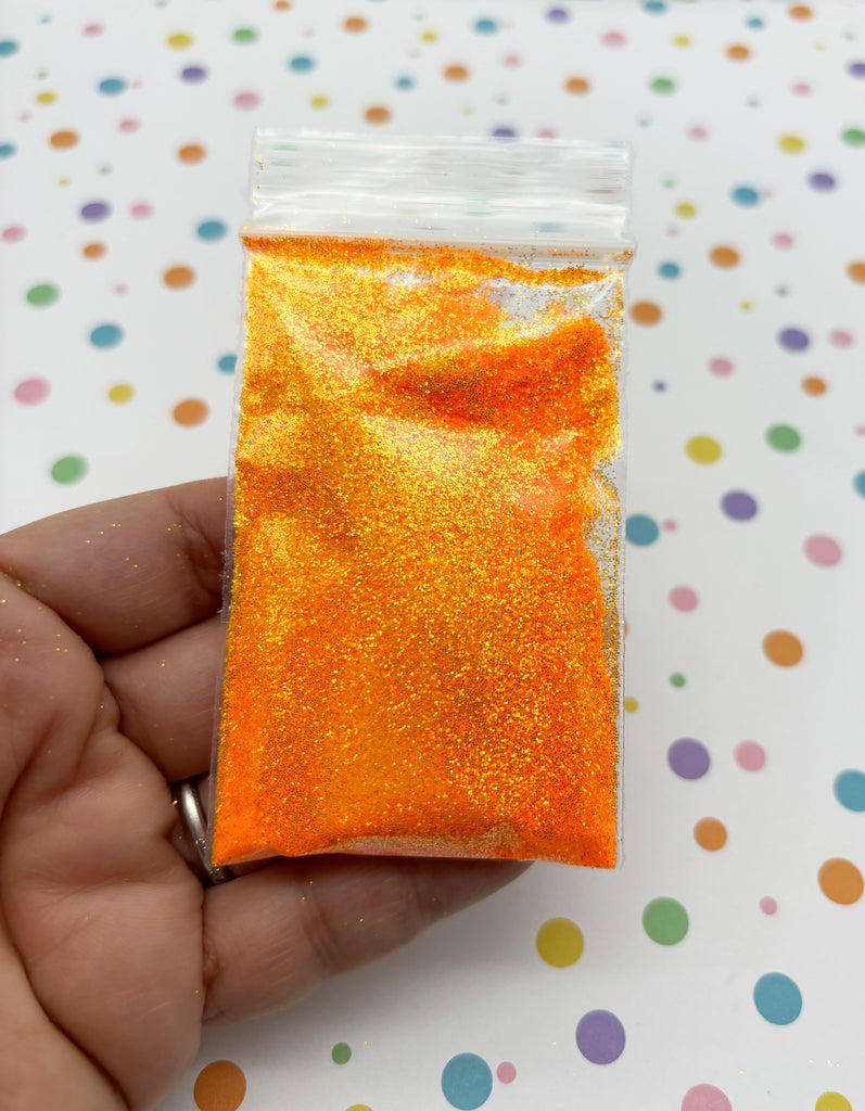 a hand holding a bag of orange glitter