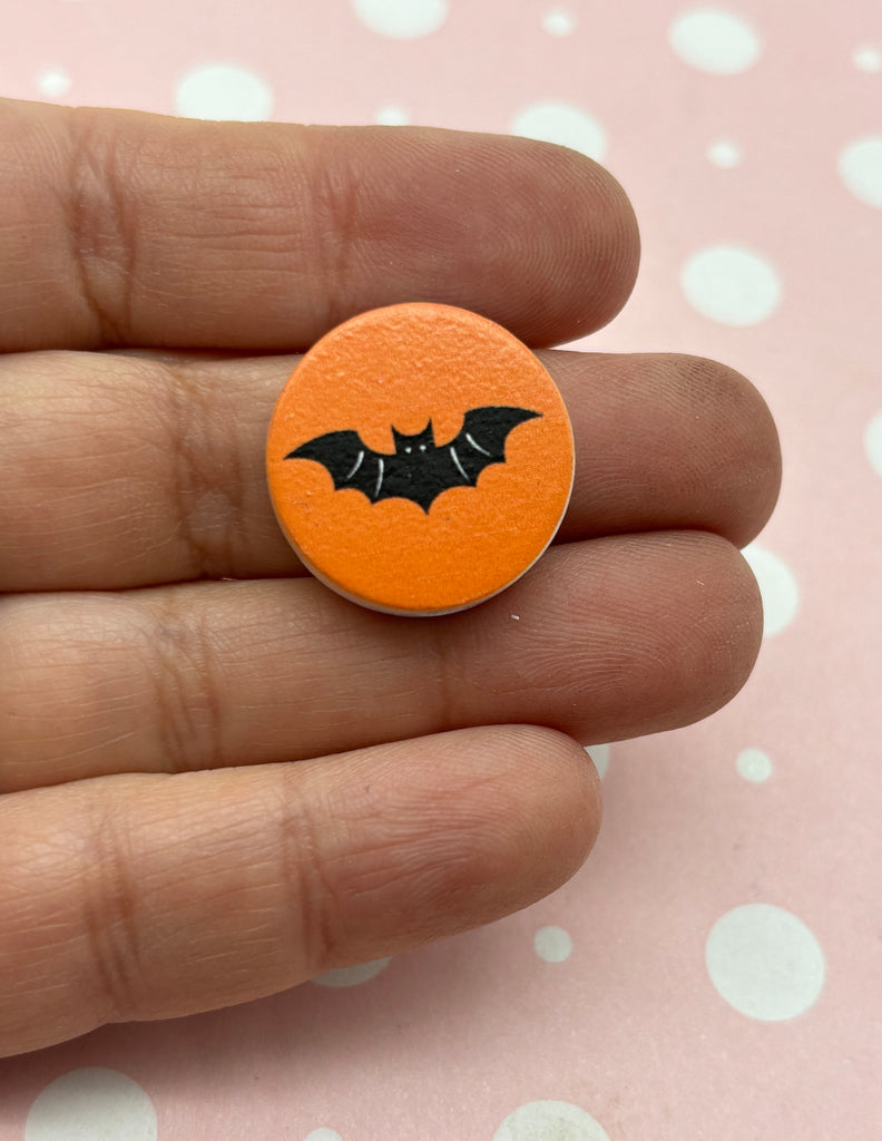 a hand holding a small orange button with a bat on it