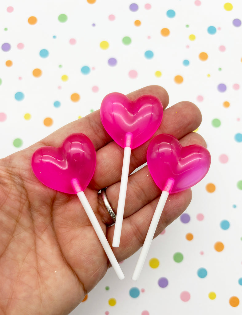 a person holding three heart shaped lollipops in their hand