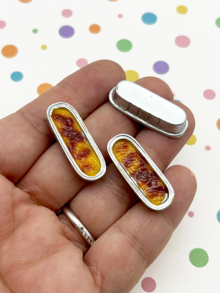 A hand holding two small, rectangular metal objects with a yellow and red color scheme, against a background with colorful polka dots.