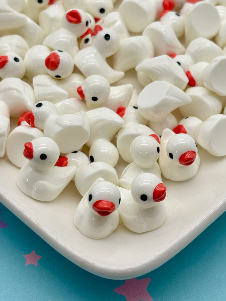 a collection of white ceramic ducks with red beaks, arranged on a white plate against a blue background with pink stars.