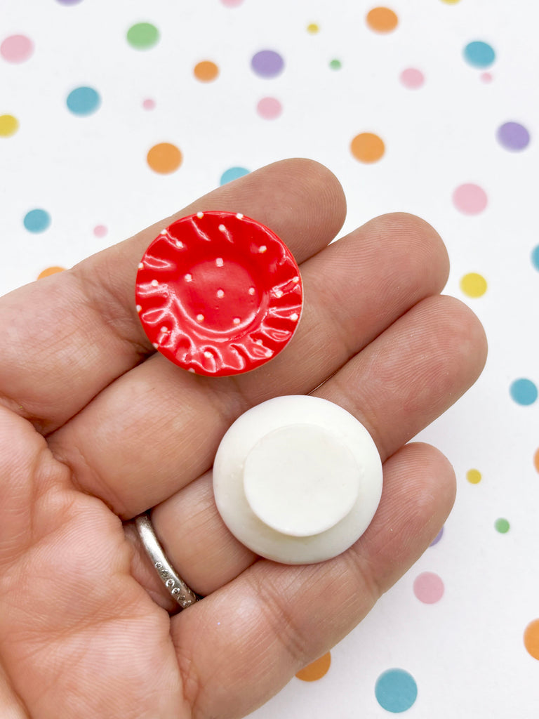 A hand holding a red and white object against a background with colorful polka dots.