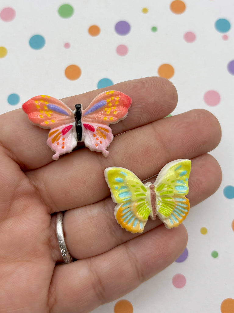 A hand holding two colorful butterfly-shaped charms against a background with polka dots.