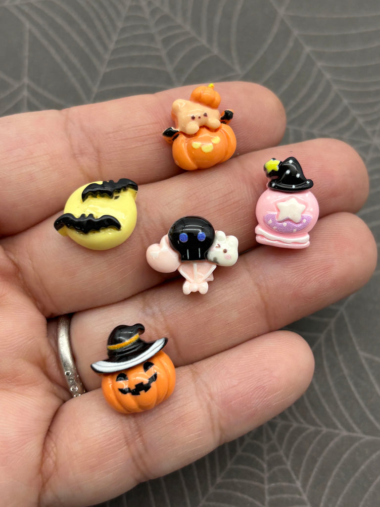 A hand holding a collection of small, colorful plastic figurines, including a pumpkin, a bat, a skull, a cat, and a witch's hat.