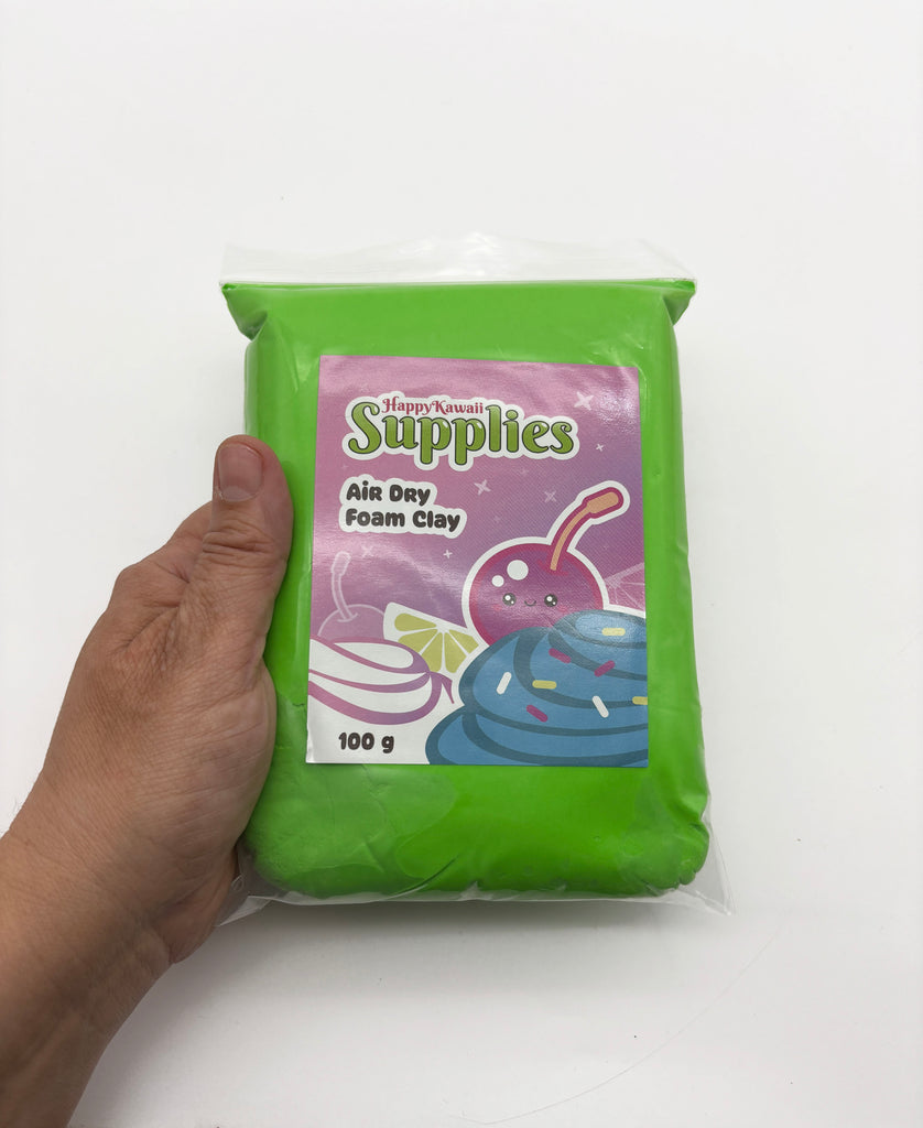 A hand is holding a package of green air day foam clay.