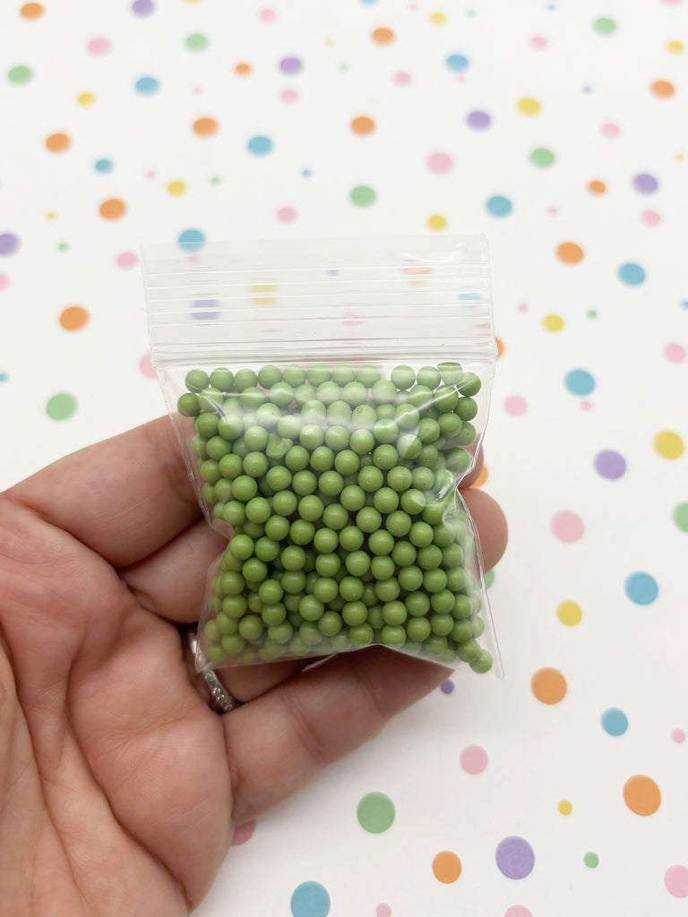 A hand is holding a small bag filled with green beads against a background with colorful polka dots.