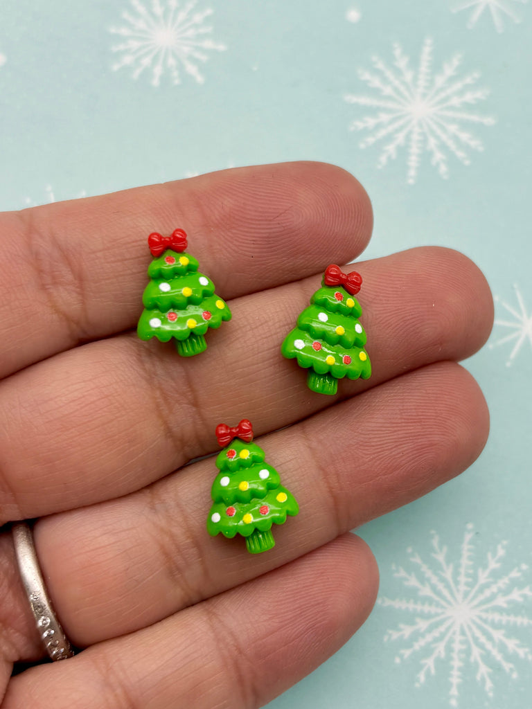 A hand holding three small green Christmas tree-shaped earrings with red bows.