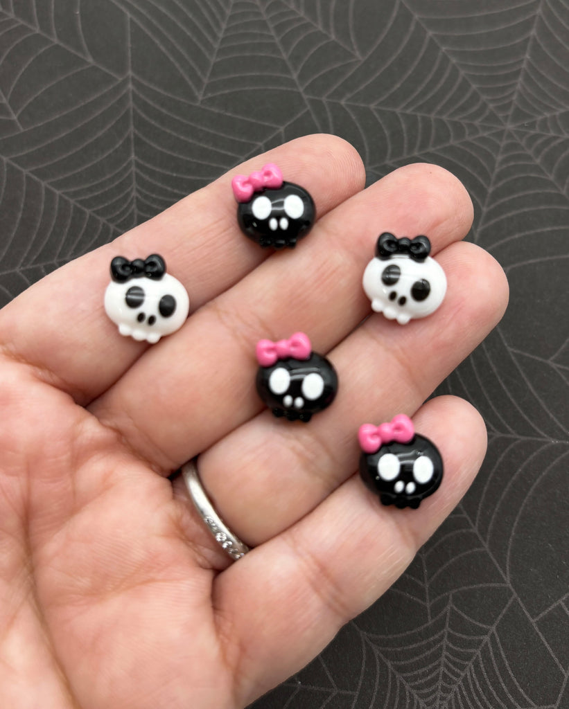A hand holding five small skull-shaped charms with pink bows on them.