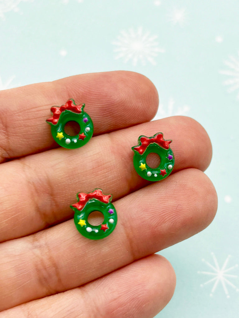 a hand holding a pair of green and red earrings