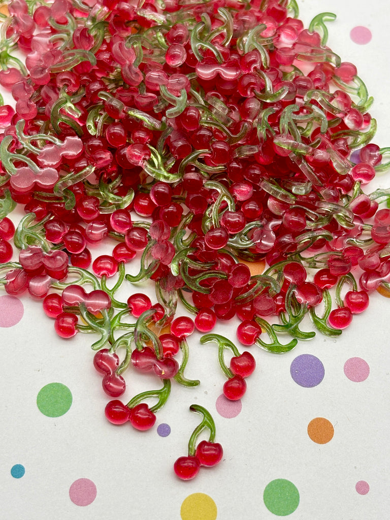 a pile of red and green plastic cherries scattered on a white background with colorful polka dots.