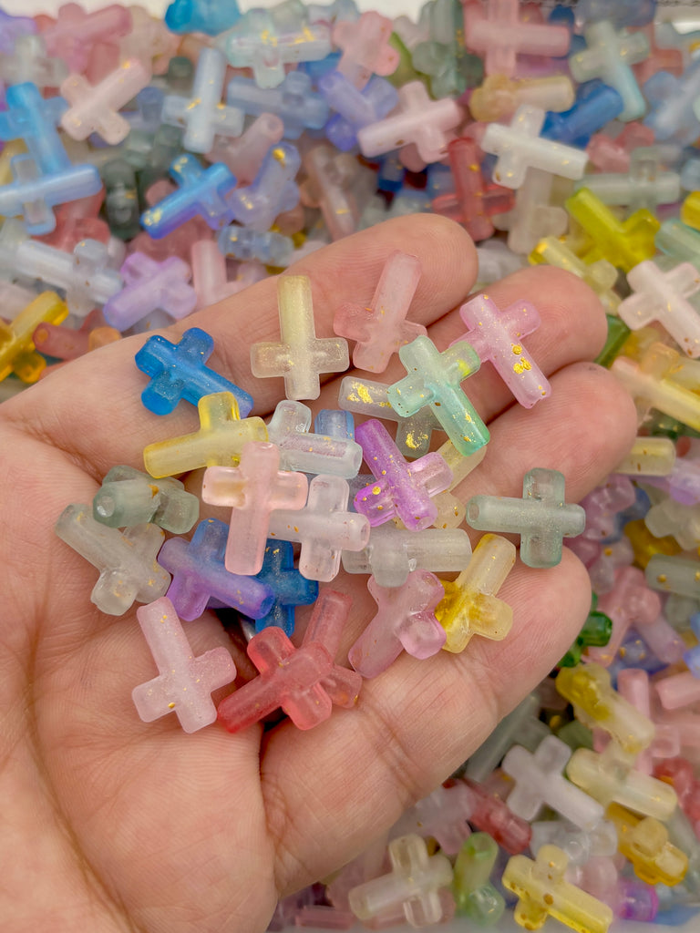 A hand holding a pile of multicolored, small, and shiny beads in various pastel shades.