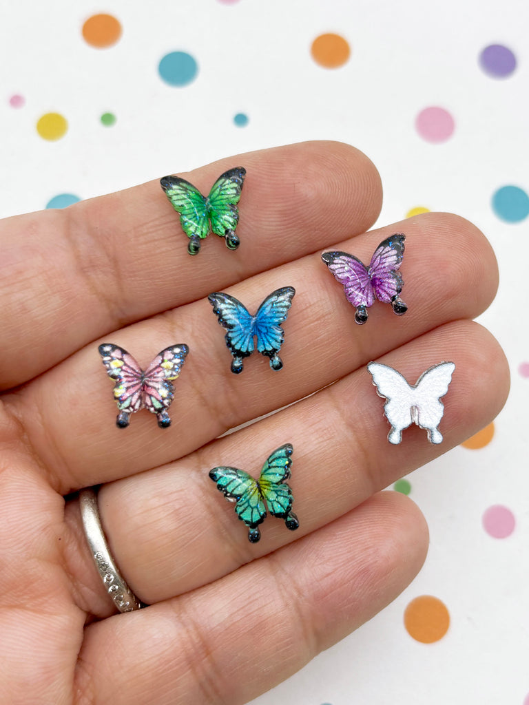 A hand holding a collection of colorful butterfly-shaped earrings against a background with polka dots.