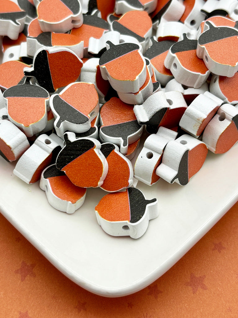 a white plate filled with numerous small wooden acorn-shaped objects in various shades of orange and black.