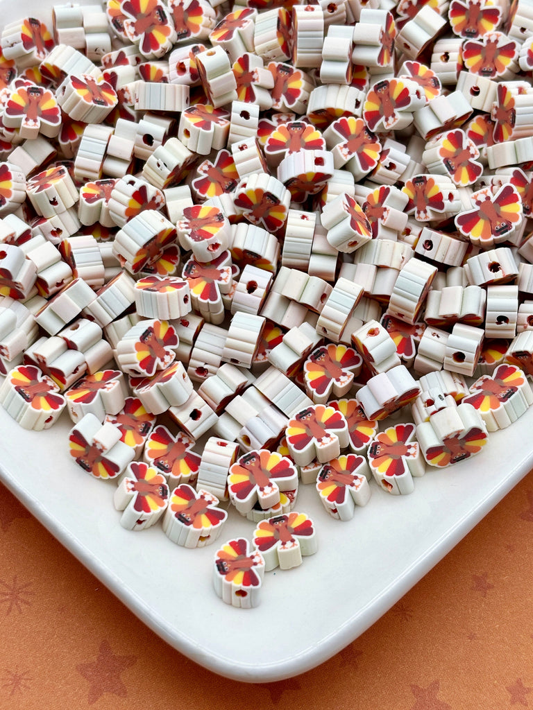 a large pile of small, colorful beads or beads with a repeating pattern of red, yellow, and white shapes, resembling a butterfly design. The beads are scattered across a white surface, creating a visually appealing and vibrant display.