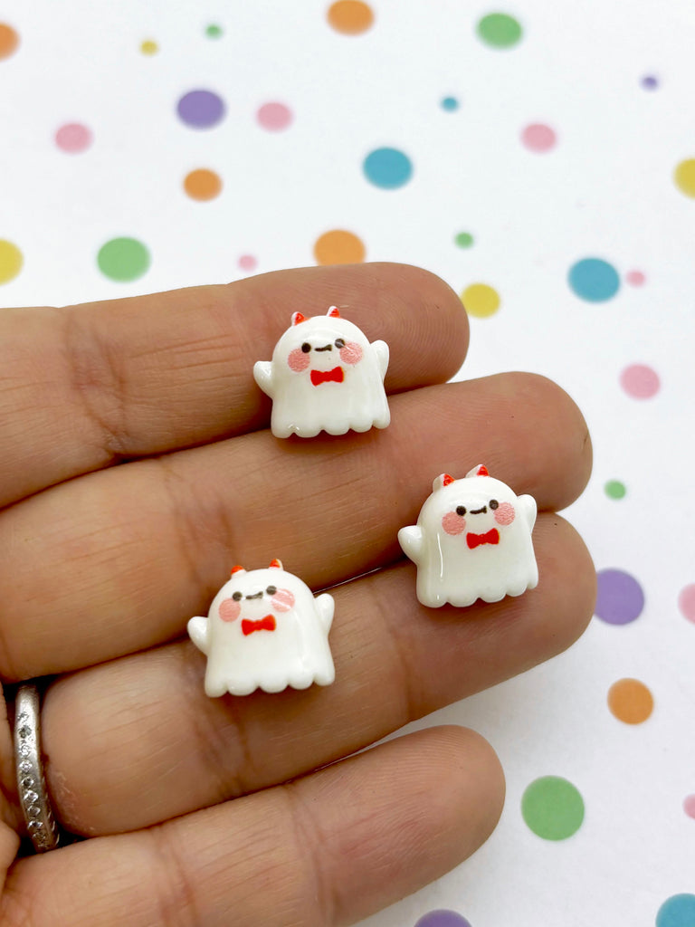 a hand holding two small white ghost earrings