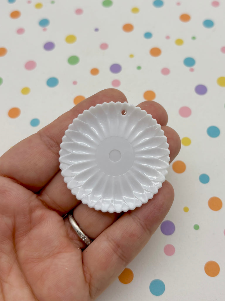 A hand holding a white, round, flower-shaped object against a background with colorful polka dots.