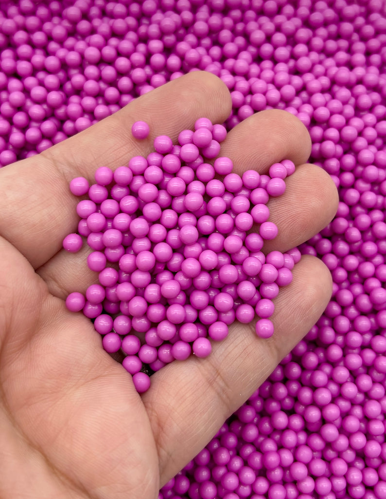 A hand holding a pile of small, round, purple beads.