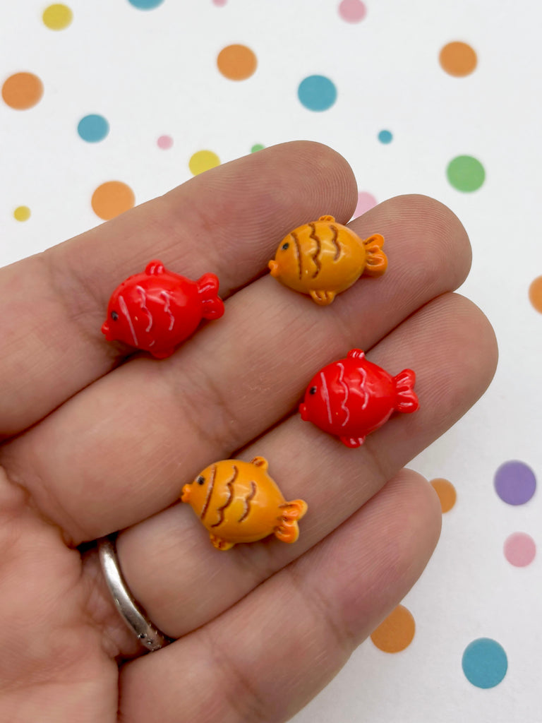 A hand holding four small, colorful fish-shaped charms against a background with polka dots.