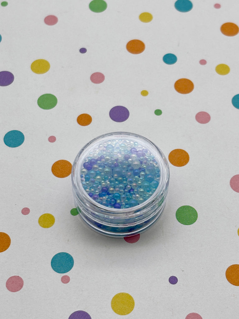 A clear container filled with small, colorful beads is placed on a white surface with a background of multicolored polka dots.