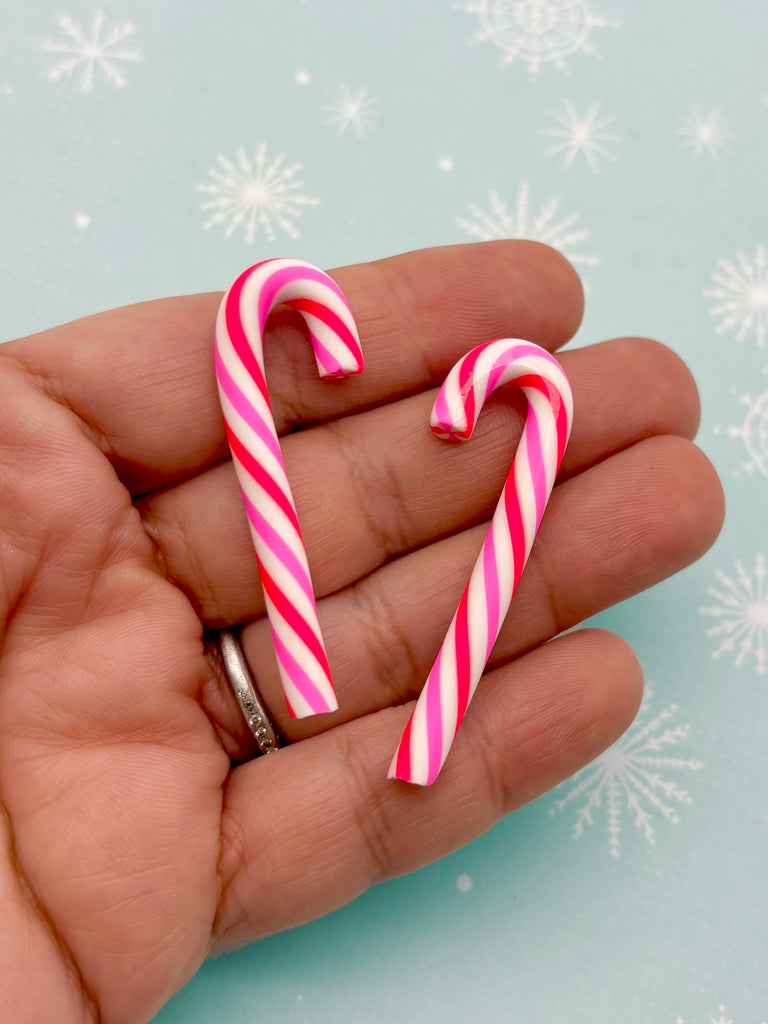 A hand holding two pink and white striped candy canes against a light blue background with white snowflakes.