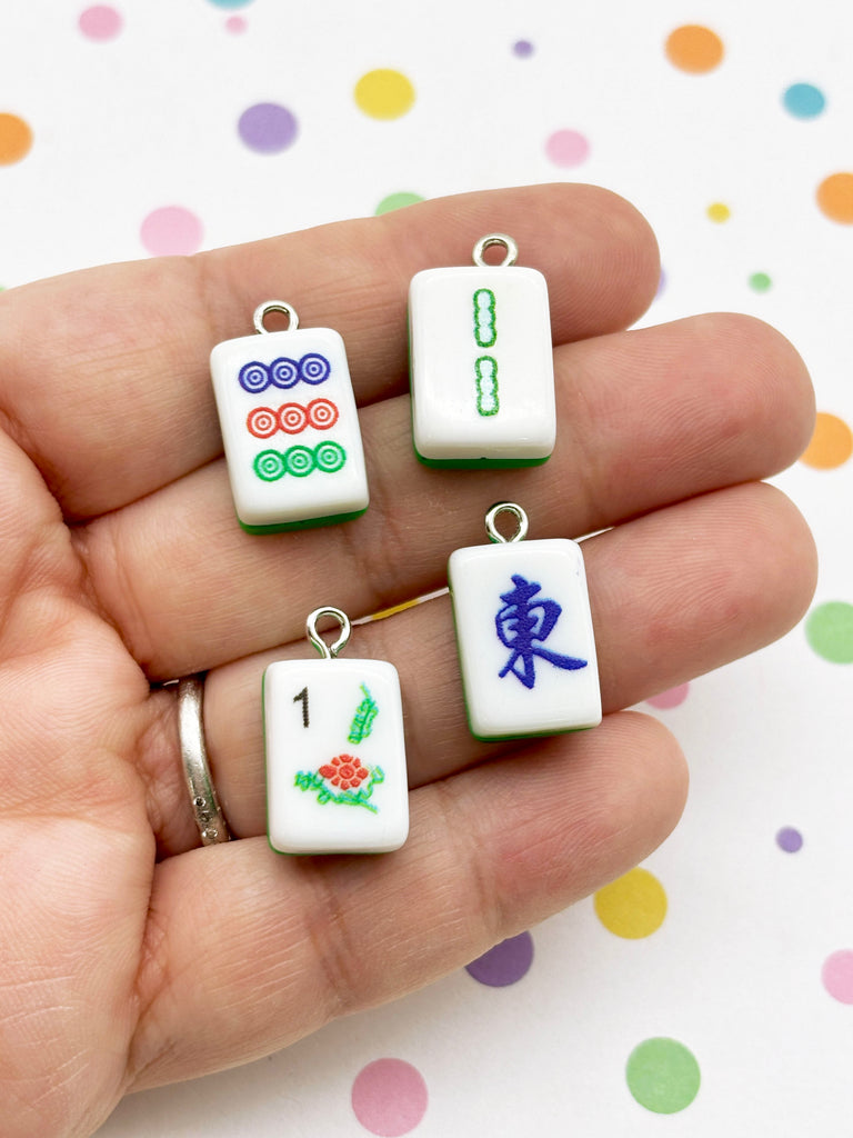 A hand holding four colorful pendants, each with a unique design, against a background with polka dots.