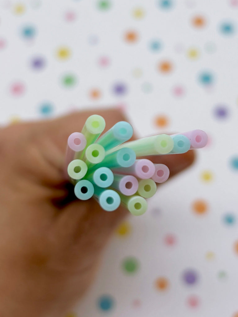 A hand holding a bunch of colorful straws against a background with multicolored dots.
