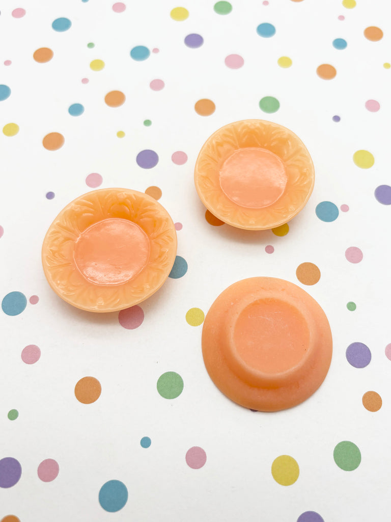 three small orange-colored bowls or containers placed on a white background with colorful polka dots.