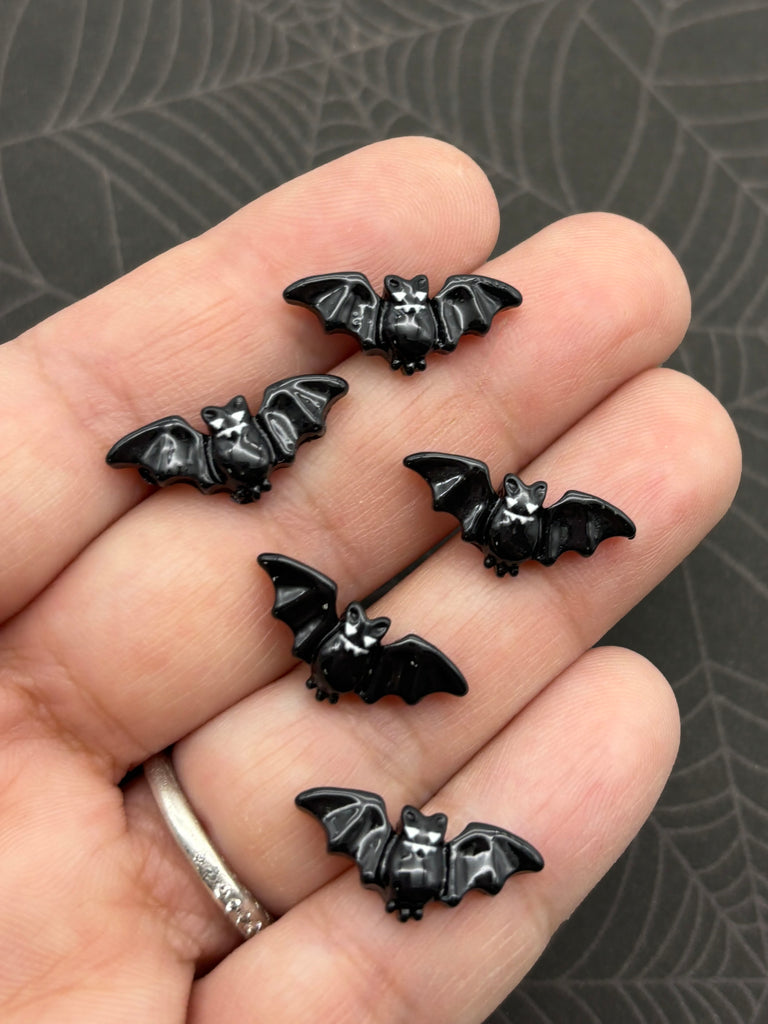 A hand holding five small black bat-shaped buttons against a dark background.