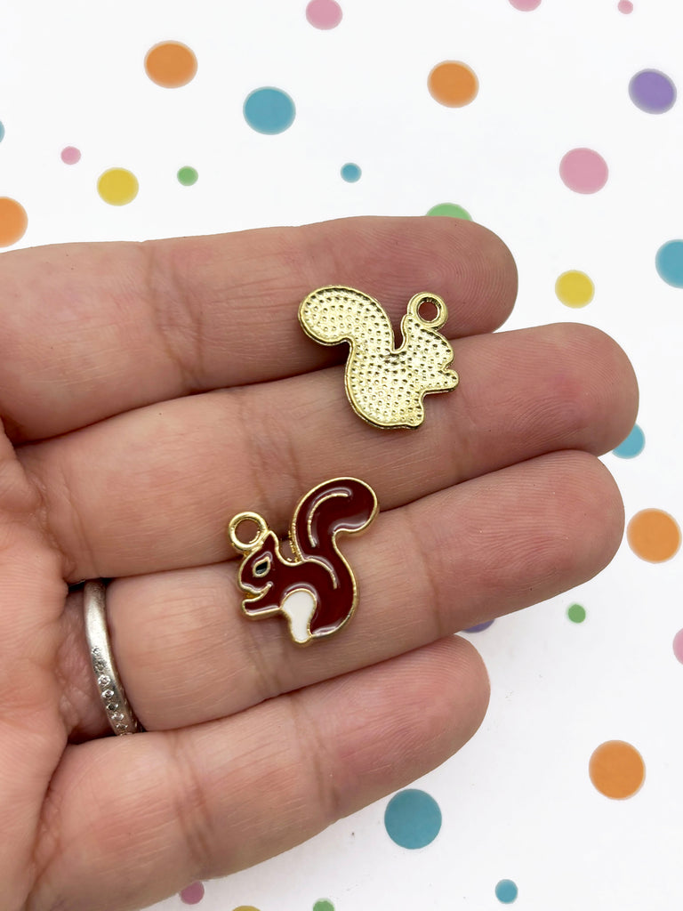 A hand holding two small, colorful pendants shaped like squirrels.