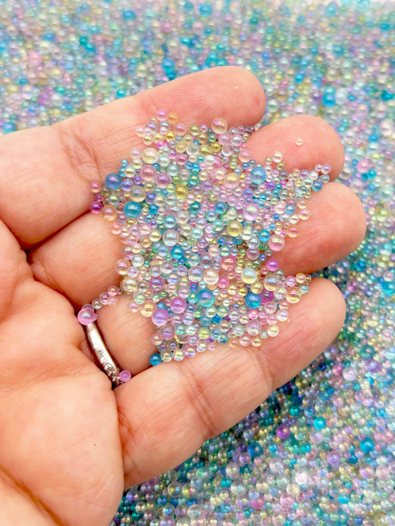 A hand holding a pile of multicolored beads against a background of colorful beads.