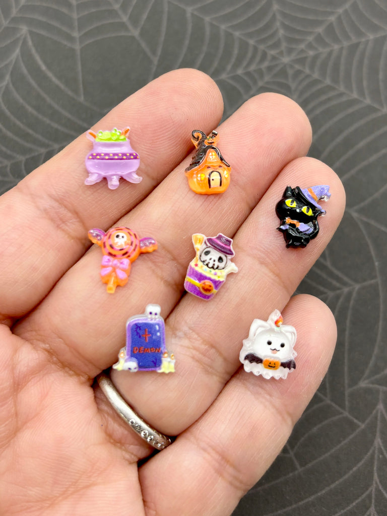 A hand holding a collection of small, colorful Halloween-themed stickers or charms on the fingers.